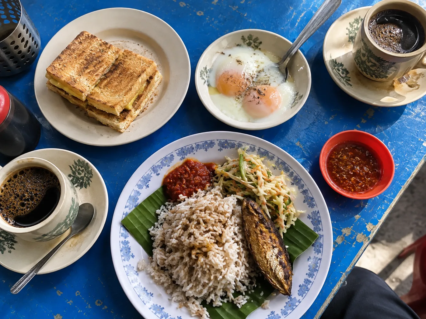 Kaya toast, eggs, nasi dagang and coffee on a blue table